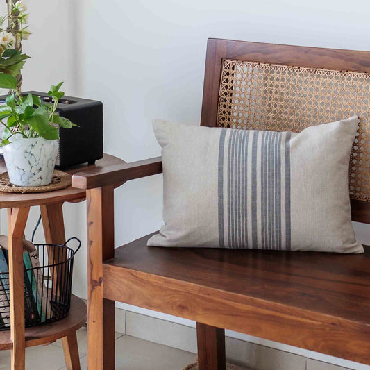 Wooden bench with a striped linen pillow, plant, and black speaker in a room.