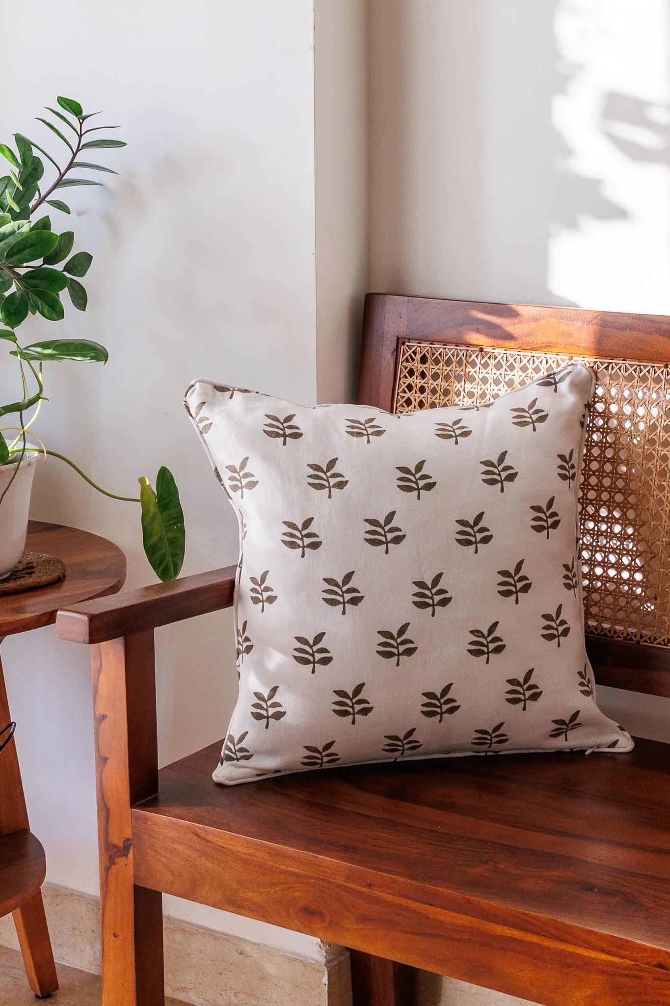 Decorative pillow with leaf pattern on a wooden bench next to a plant