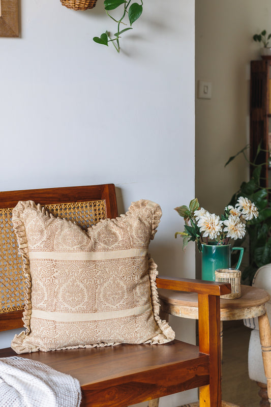 Rust Block print pillow on a wooden chair with a side table and flowers in the background