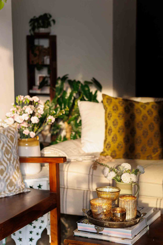 A living room set up with cushions, flowers , plants and books