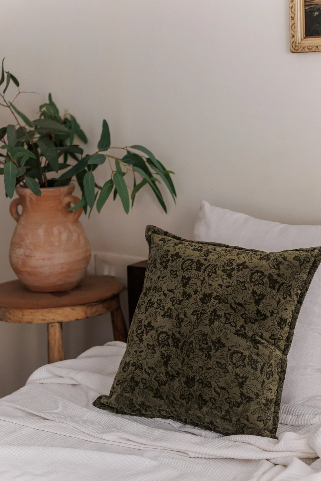 Forest Green Velvet Cushion Cover on a Bed with a Terracotta Vase and leaves inside it