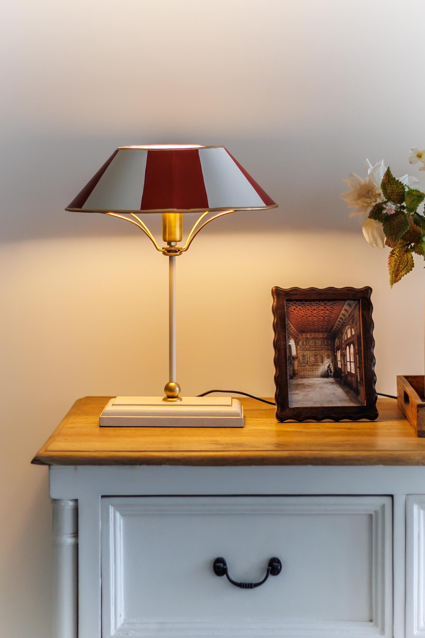 Table lamp with a red and white striped shade on a wooden surface next to a framed picture.