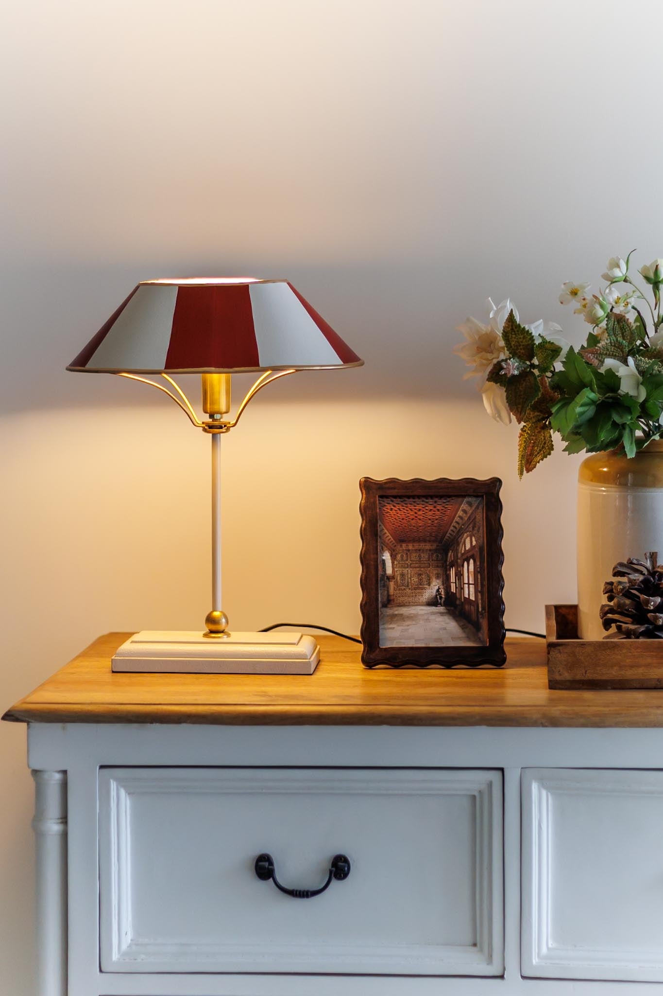 Table lamp with a red and white shade on a wooden side table with decorative items.