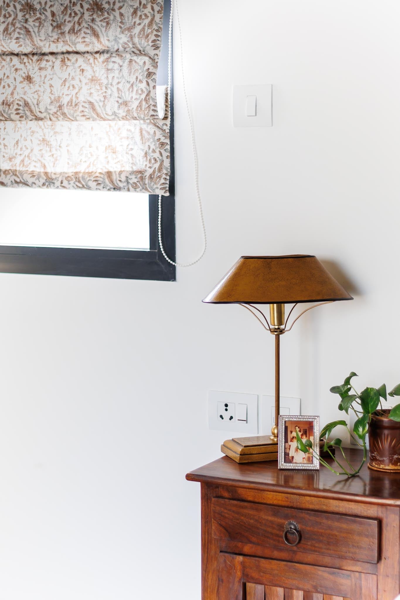 Wooden side table with lamp, books, and plant against a white wall.
