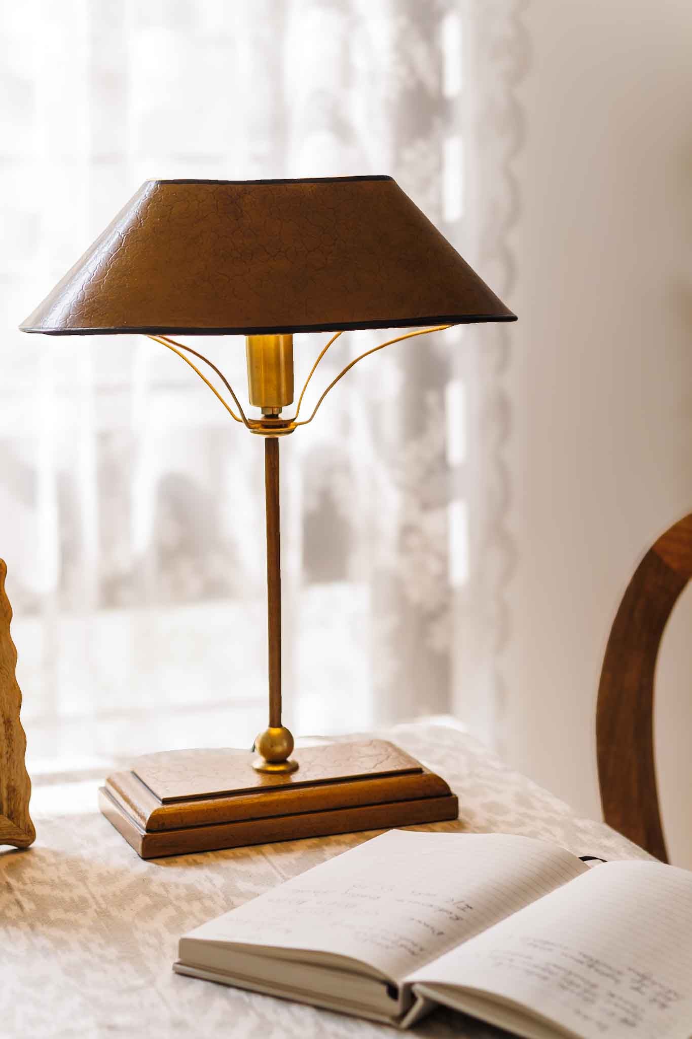 Decorative table lamp with a brown shade on a surface next to an open book.