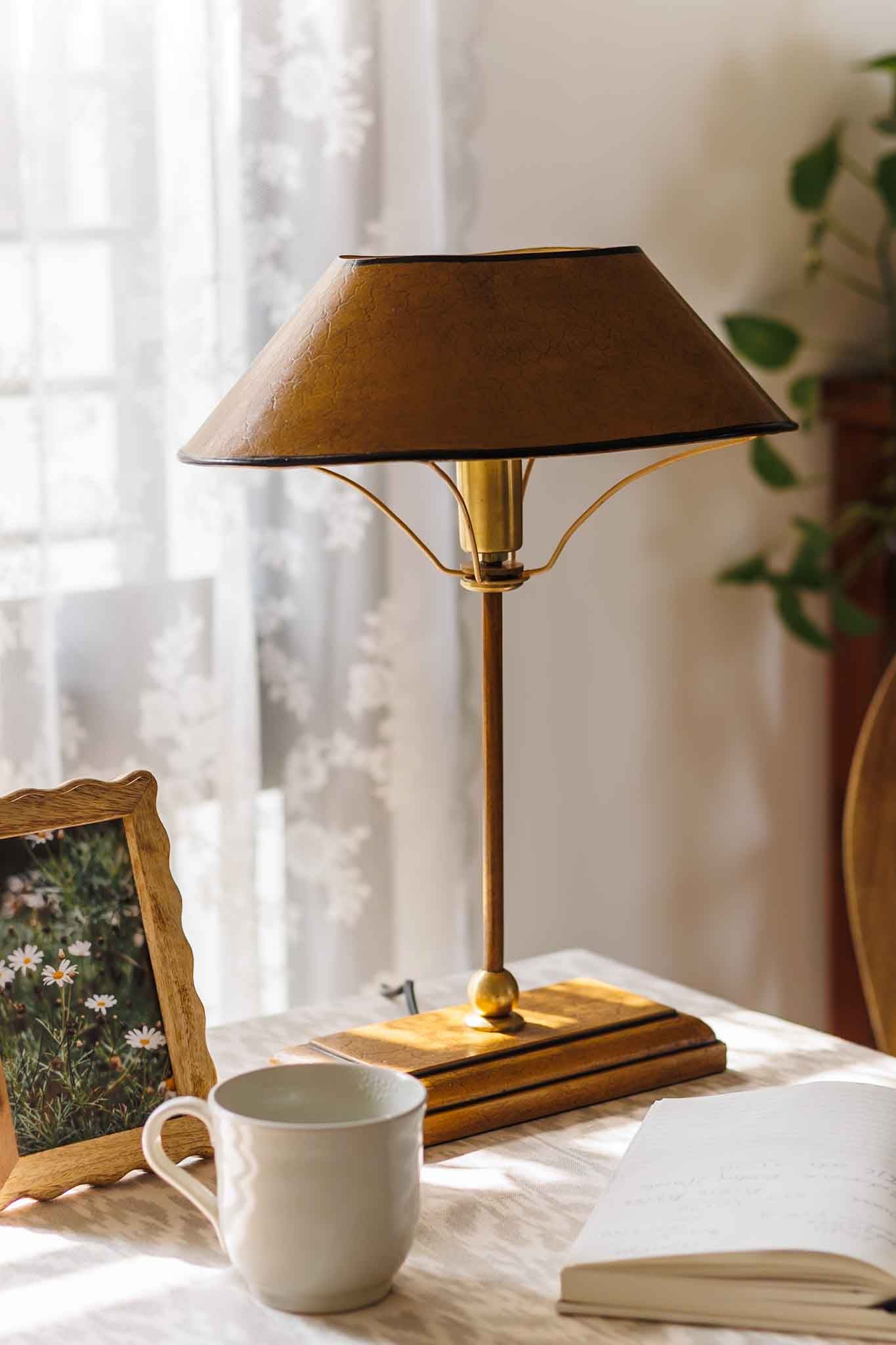 Vintage-style table lamp on a surface with a mug and photo frame in a softly lit room.