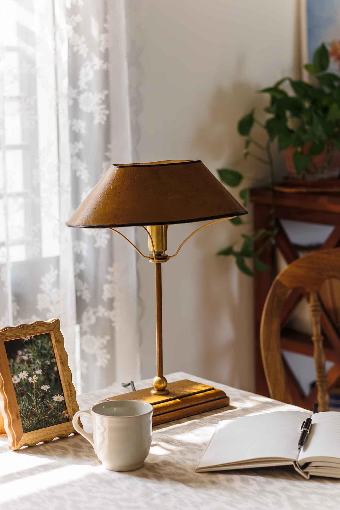 Gold lamp on a table with a cup, notebook, and pen in a cozy room setting.