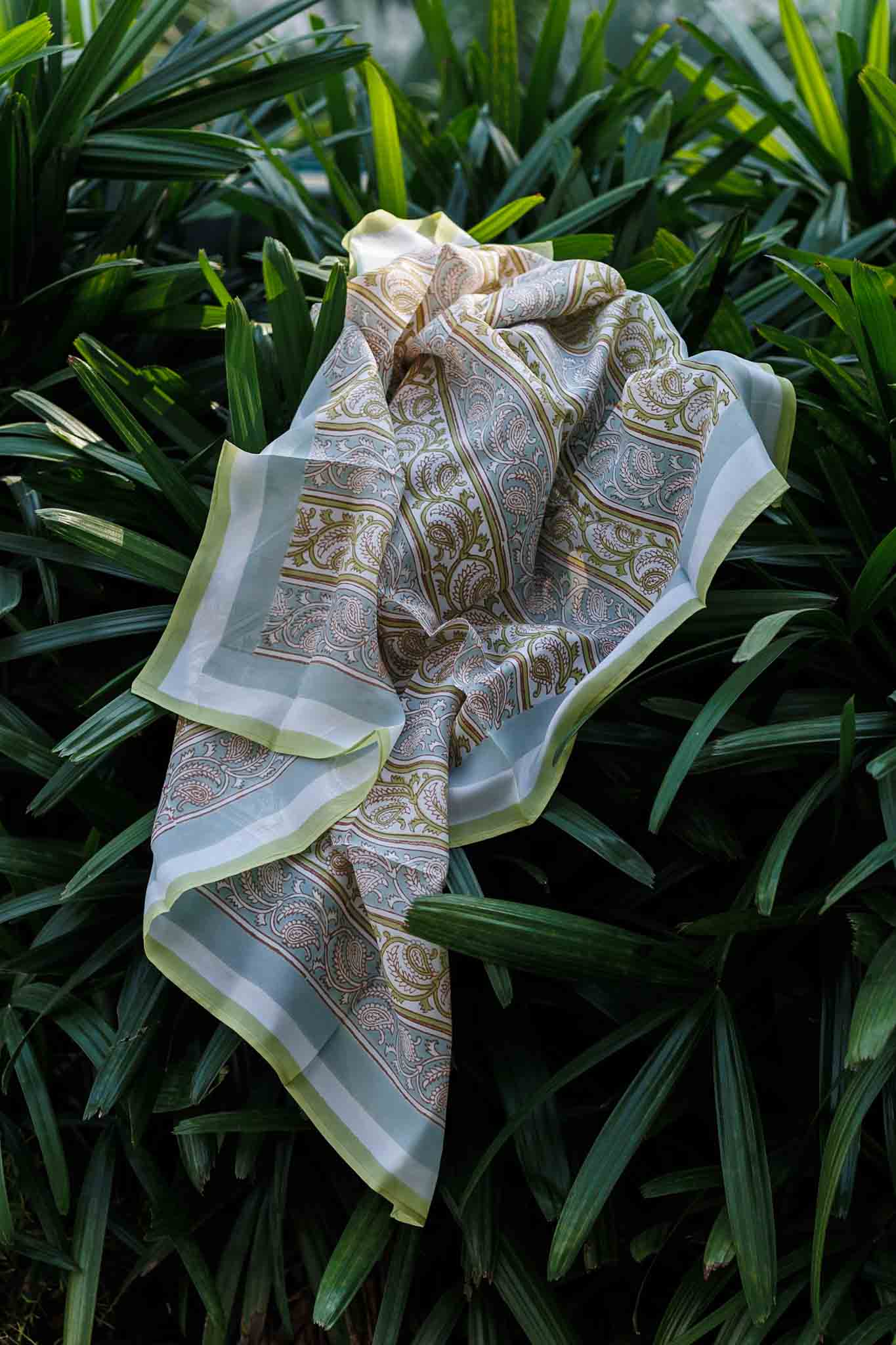 Hand block printed Habutai silk scarf in pastel lime and sage paisley pattern displayed outdoors