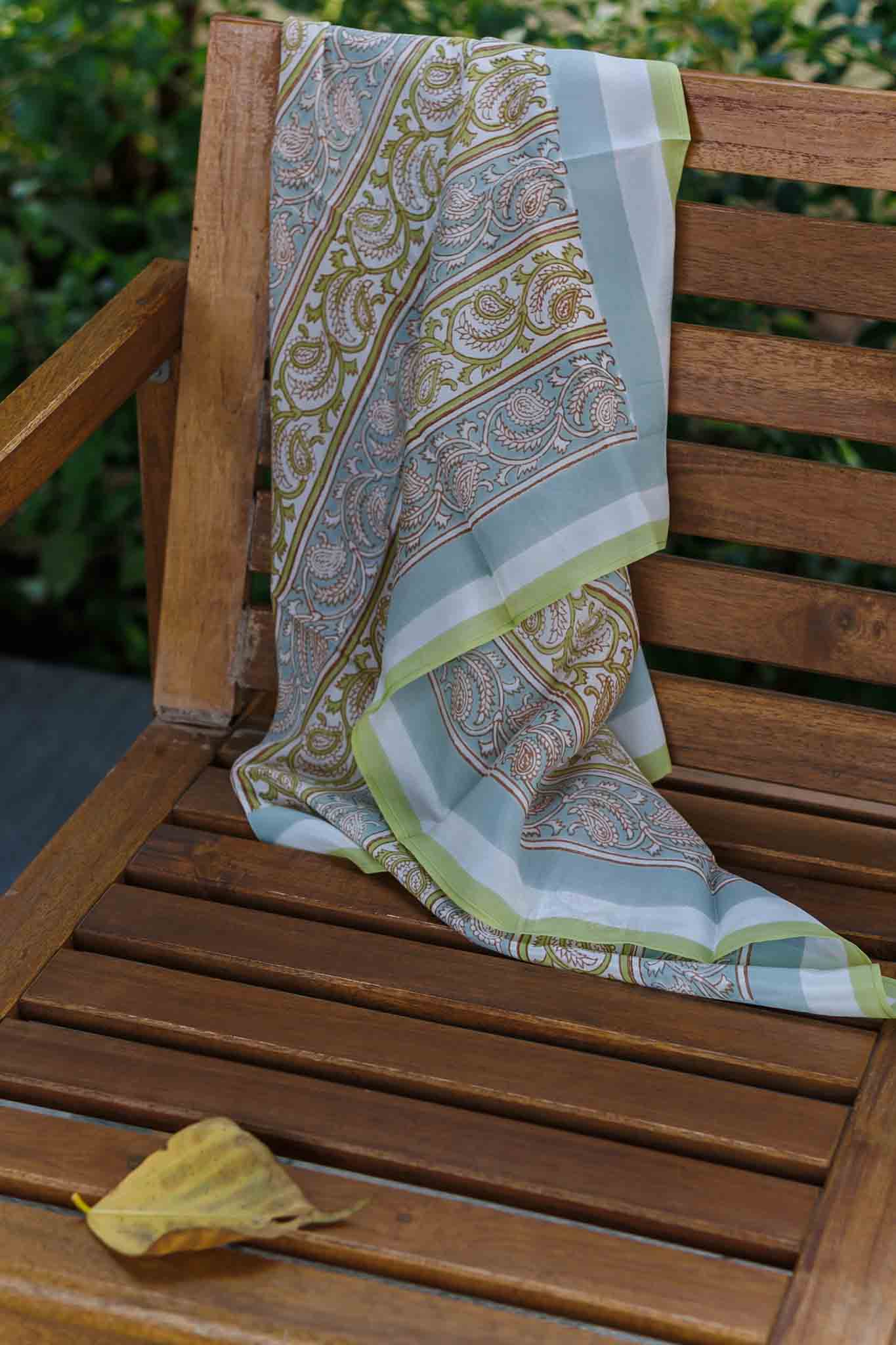 Decorative block print silk scarf with paisley pattern draped over a wooden chair outdoors.