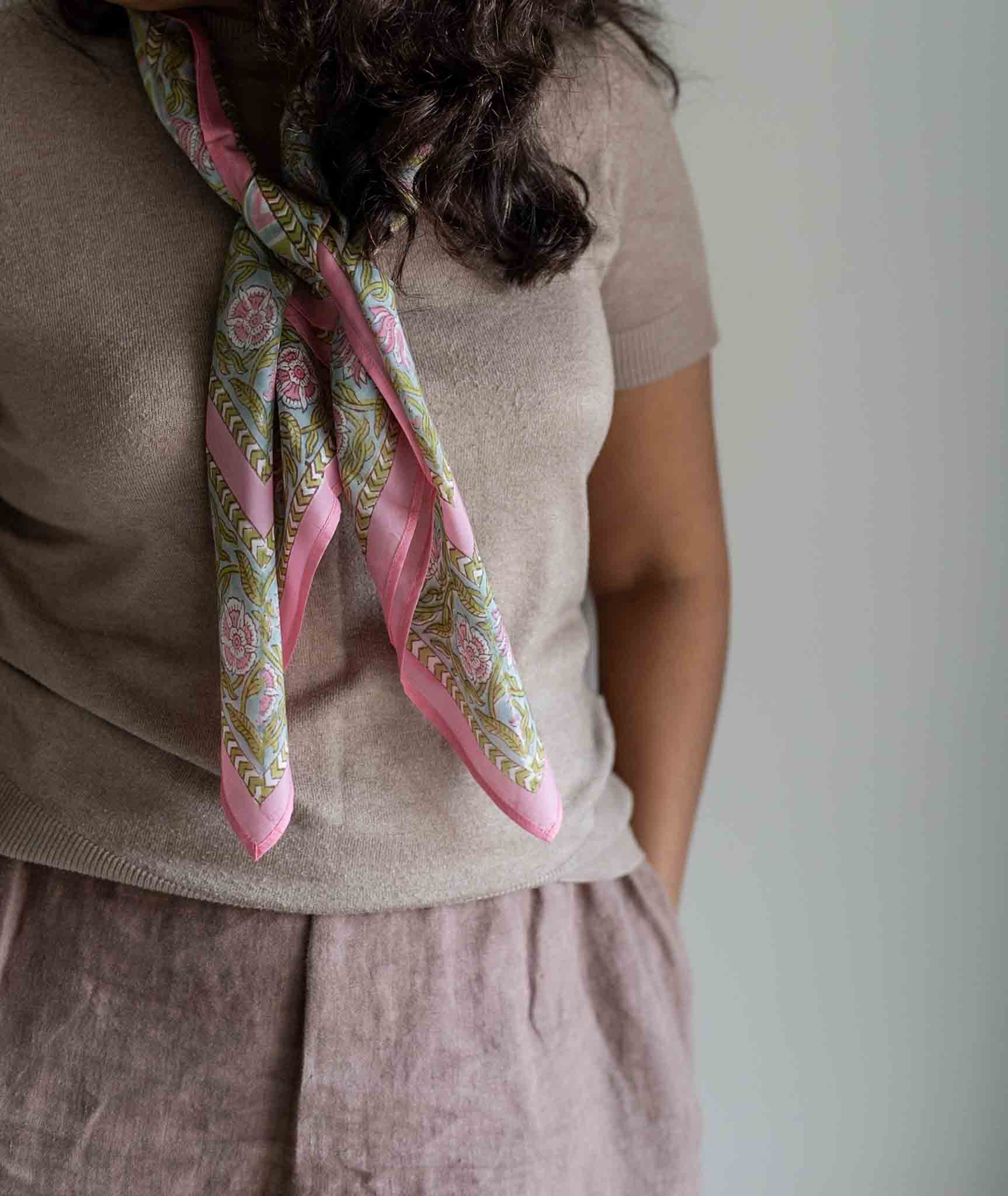 Person wearing a patterned pink scarf on a plain background