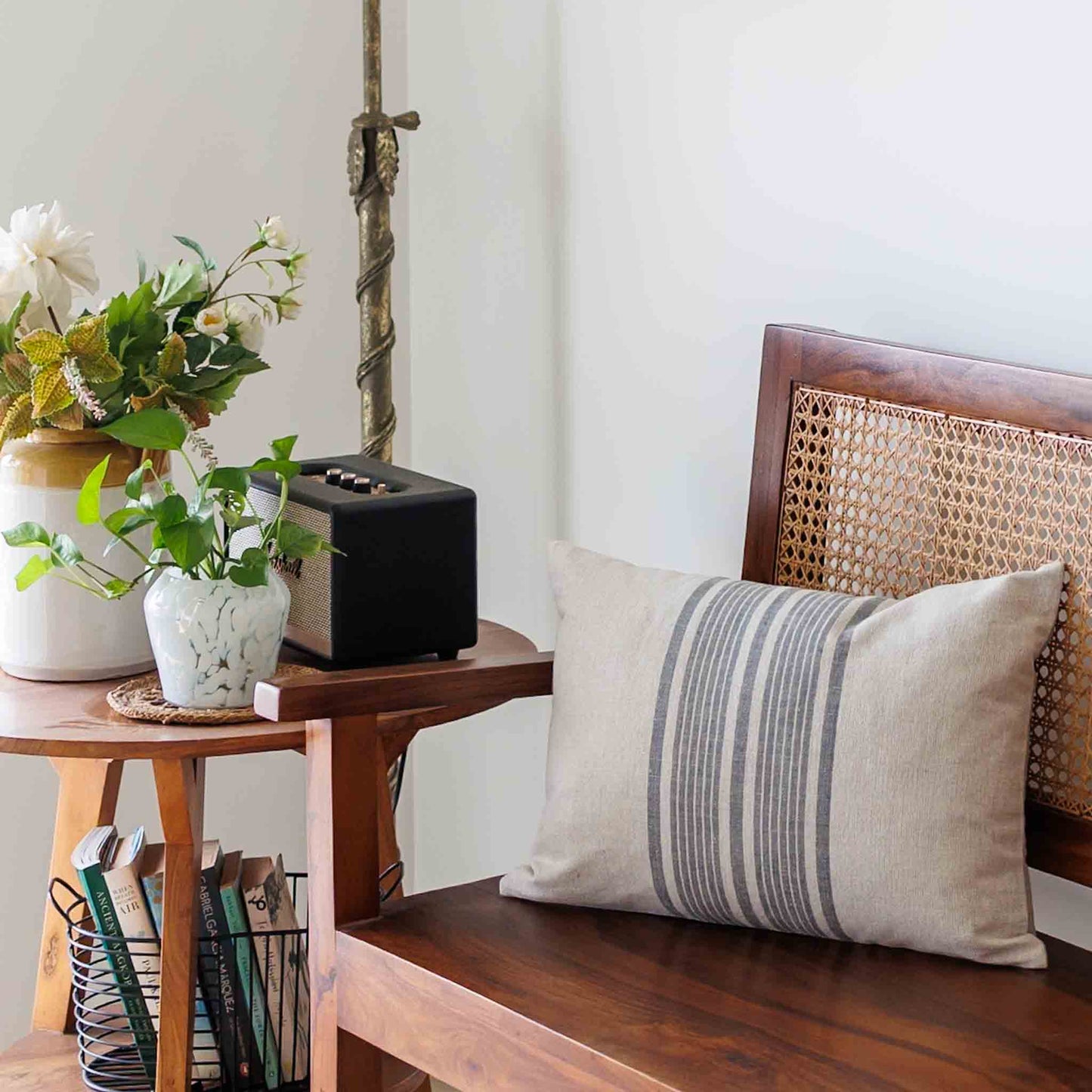 Decorative linen pillow with striped pattern on a wooden bench with plants and books in the background.