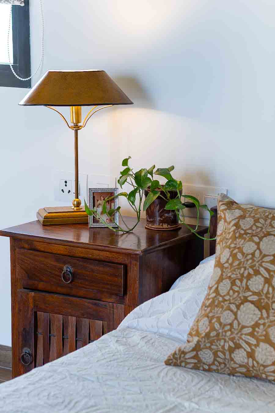 A bedroom table lamp with a conical shade sits on a dark wood bedside table 