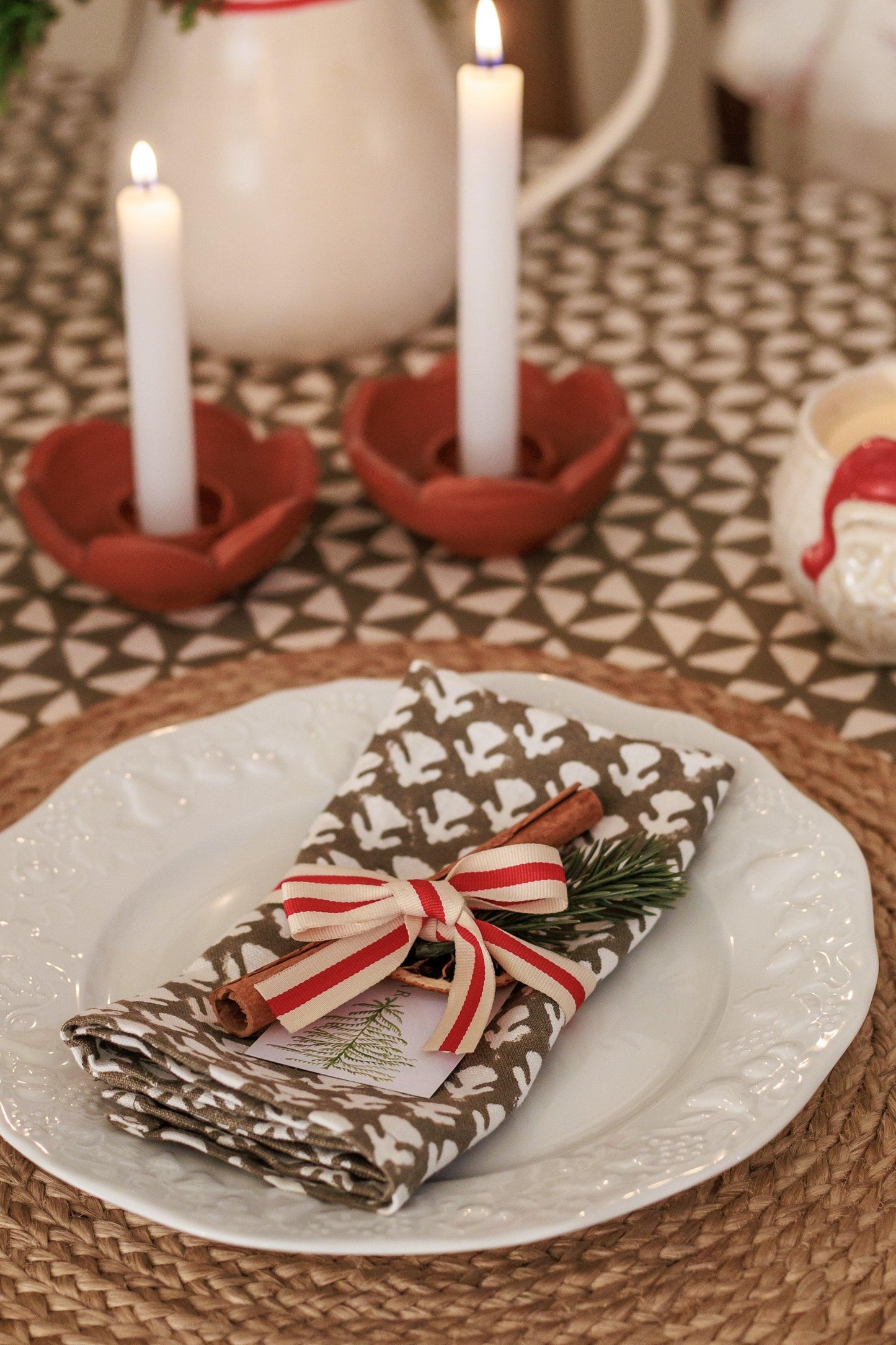 Christmas-themed table setting with candles, napkin, and decorative elements on a patterned tablecloth.