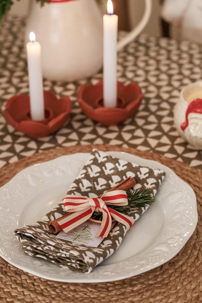 Christmas-themed table setting with candles, napkin, and decorative elements on a patterned tablecloth.
