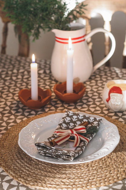 Candlelit table setting with a plate, napkin, and decorative elements on a patterned tablecloth.