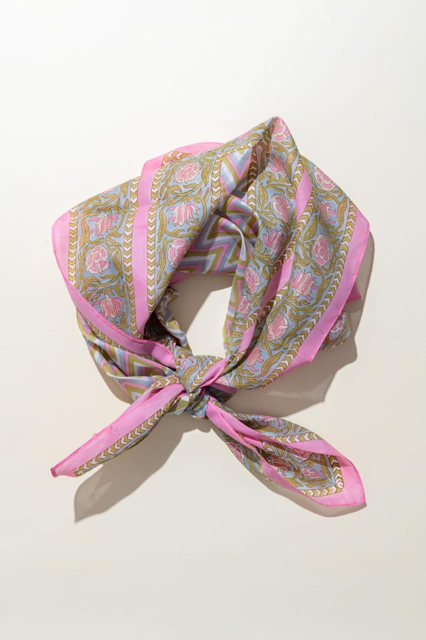 A pink patterned silk scarf with gold and blue details, tied in a knot and displayed on a light beige background.