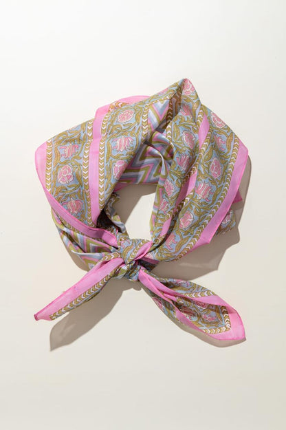 A pink patterned silk scarf with gold and blue details, tied in a knot and displayed on a light beige background.