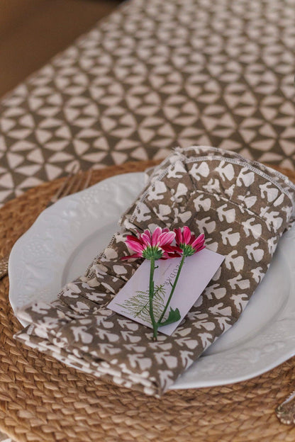Brown patterned napkin with a pink flower on a white plate on a textured surface