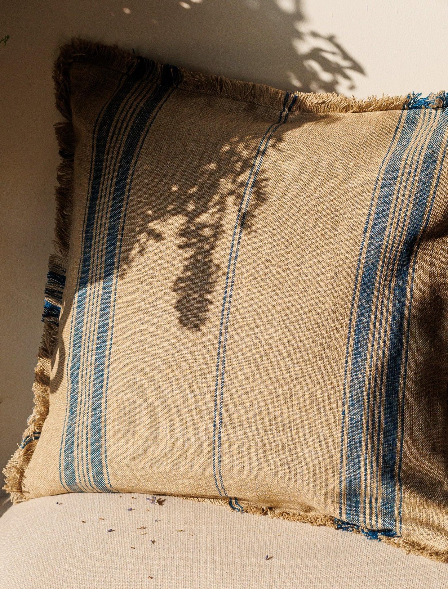 Blue stripes Linen Cushion Cover resting against a wall with sun and shadow over it