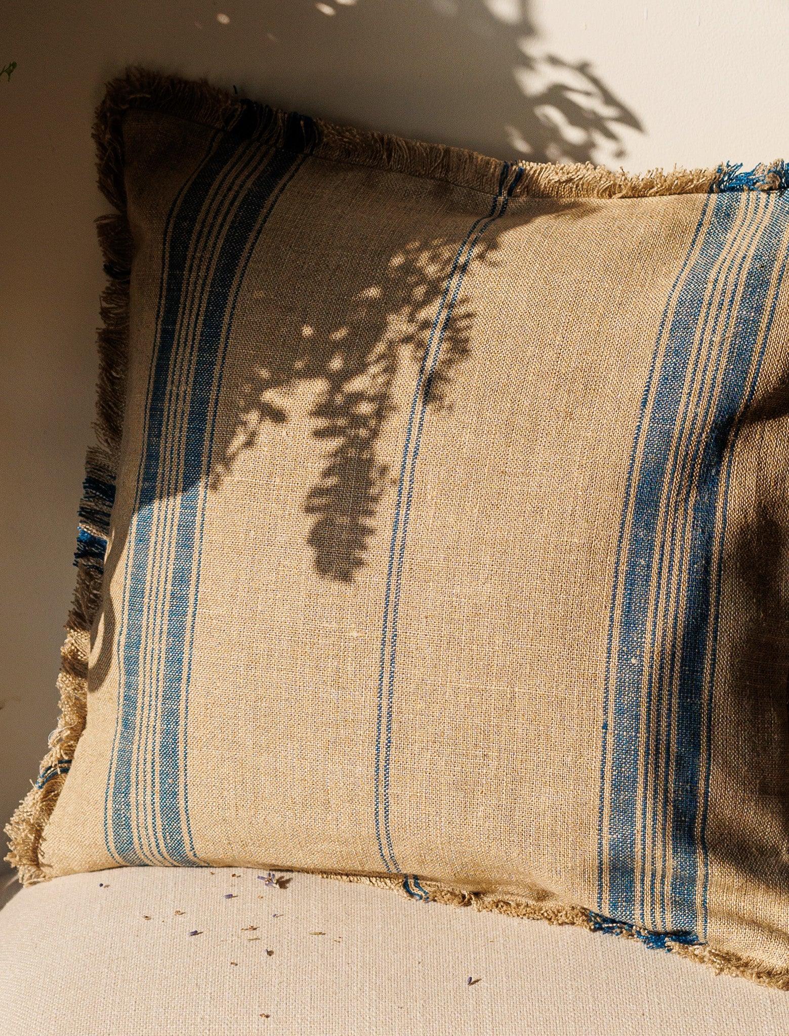 Blue stripes Linen Cushion Cover resting against a wall with sun and shadow over it