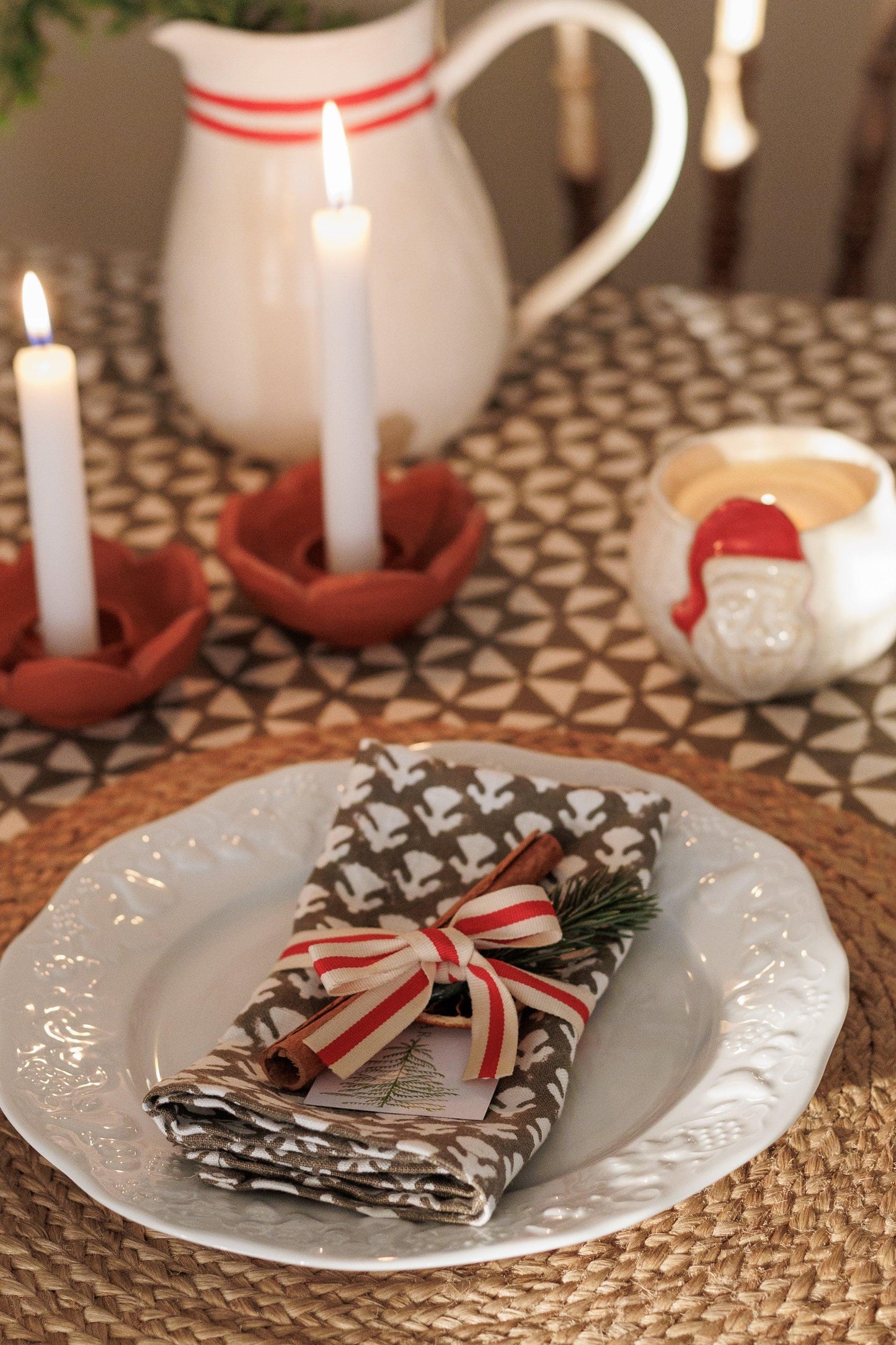 Decorative table setting with a plate, napkin, candles, and a pitcher.