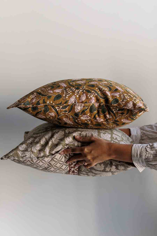 Two block print autumn decorative cushions stacked in the air, with a person's hands visible holding the pillows. 