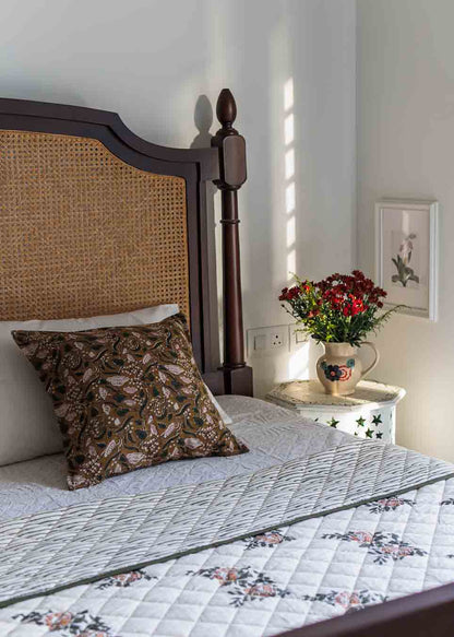 A cosy indian bedroom featuring a four-poster bed dressed in a floral quilted bedspread and a brown block print cushion cover.