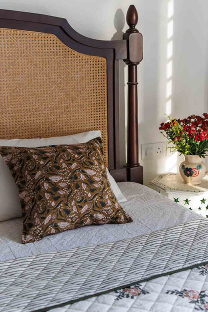 A styled bedroom scene featuring wood and woven cane headboard, a patterned brown accent pillow, and a quilted green bedspread.