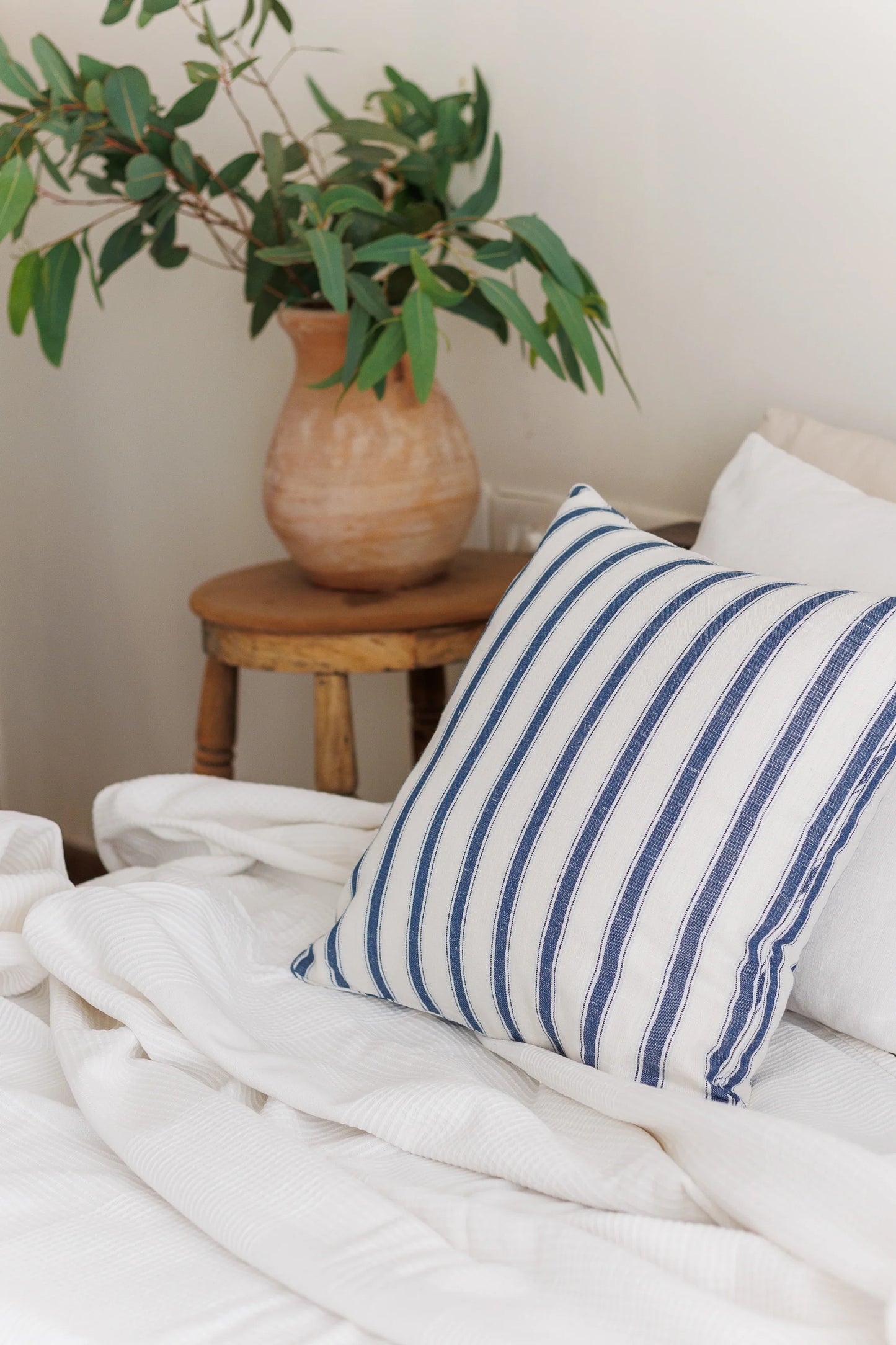 Striped blue pillow on a bed with a plant in the background
