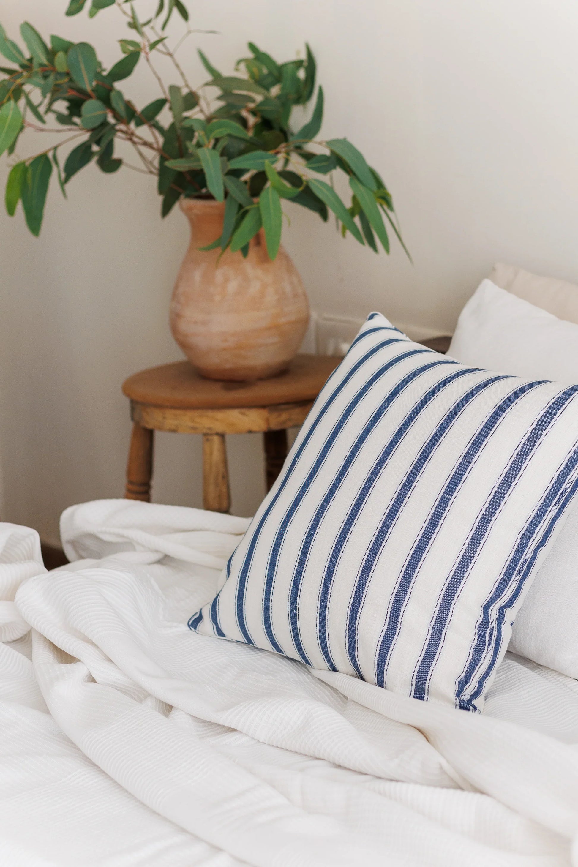 Striped blue pillow on a bed with a plant in the background