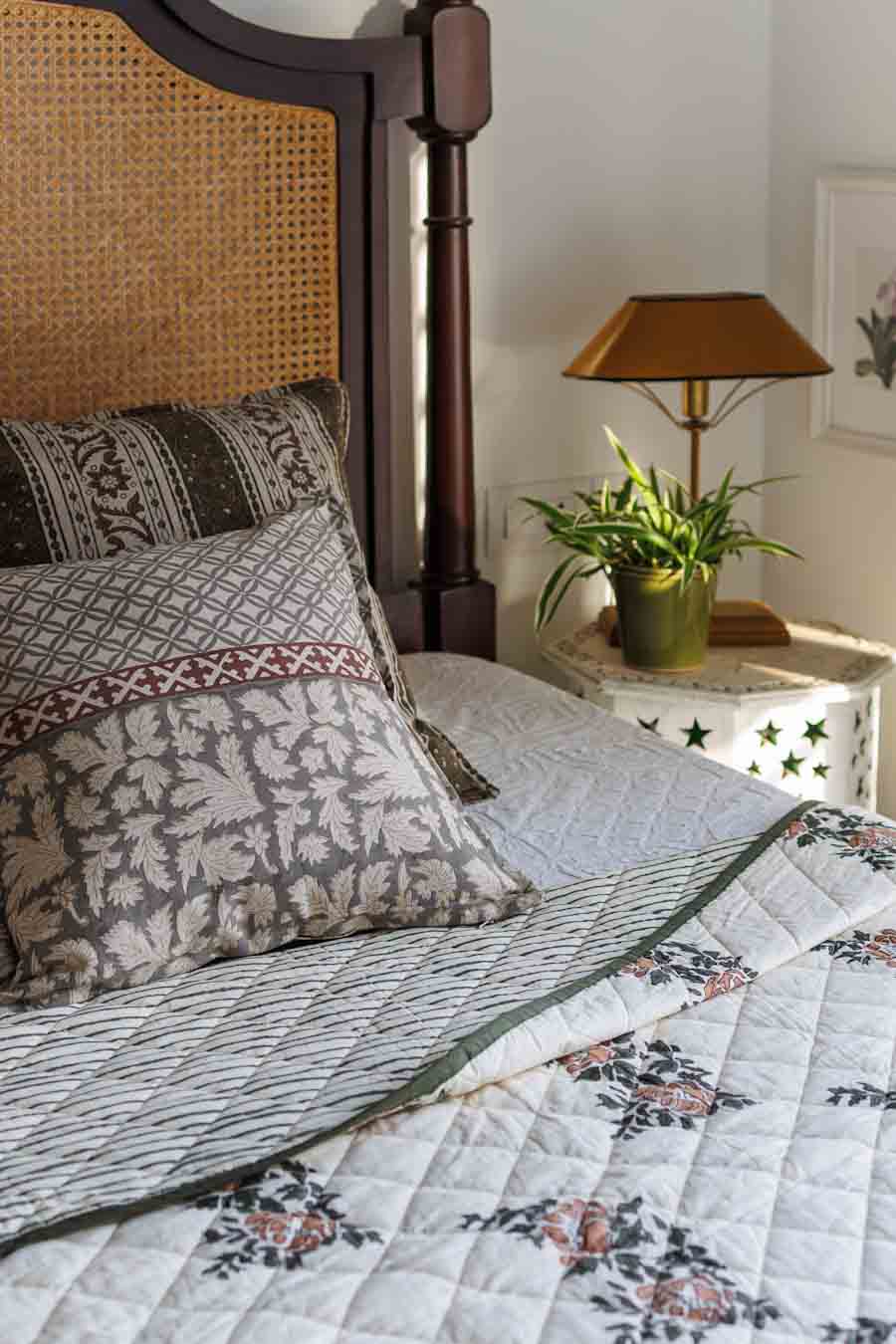 A bed with  a quilted bedspread in floral patterns with block print cushions.