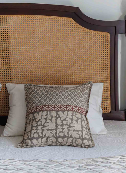 Grey block print cushion cover with a brown and beige botanical pattern and a red accent band, styled on a bed.