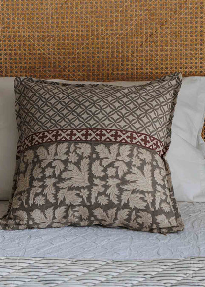 A printed cushion cover with a two-tone pattern, featuring a geometric  design on the upper half and intricate floral  motif on lower half, separated by a rust band. 