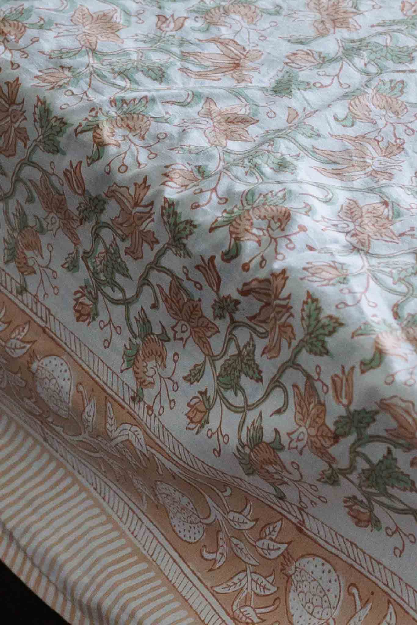 A close-up of honey suckle block printed bed sheet, featuring a cream background with a detailed botanical pattern in muted green and peach, finished with a decorative peach border.