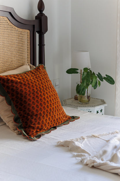 Orange patterned cushion on a bed with a nightstand and lamp in the background