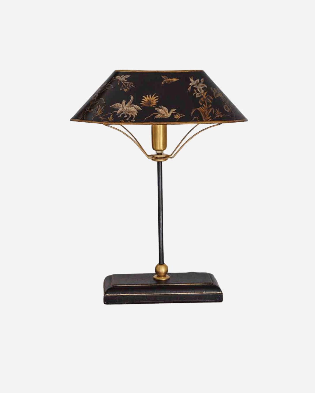 A vintage-style table lamp with a black shade decorated with gold floral motifs, supported by a gold-toned metal frame and a dark rectangular base.