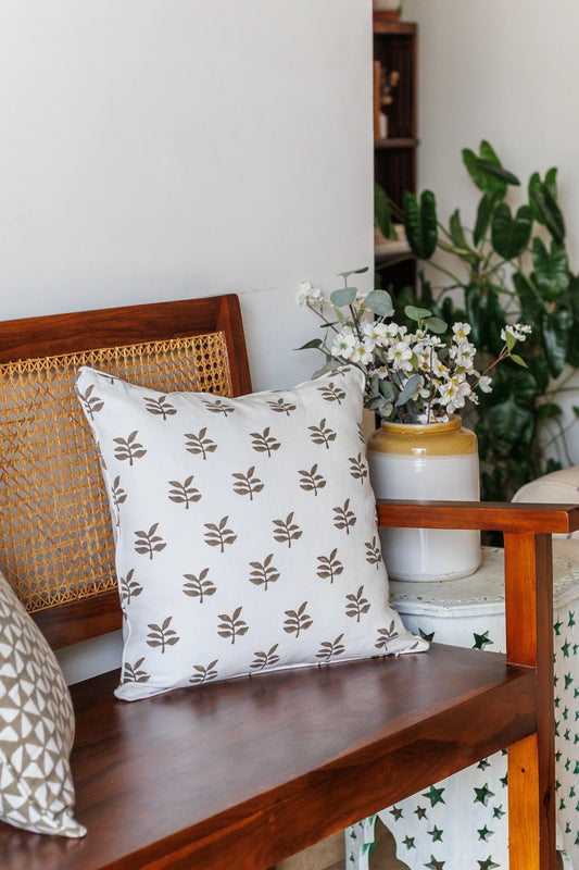 Decorative pillow with leaf pattern on a wooden bench with plants in the background