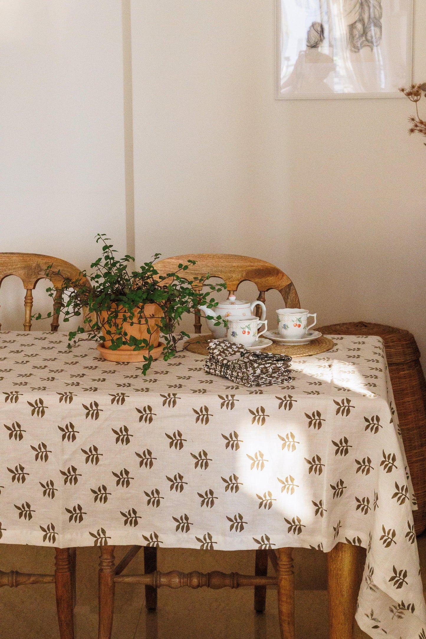 Dining table with a patterned tablecloth, teapot, and cup, set against a neutral wall.