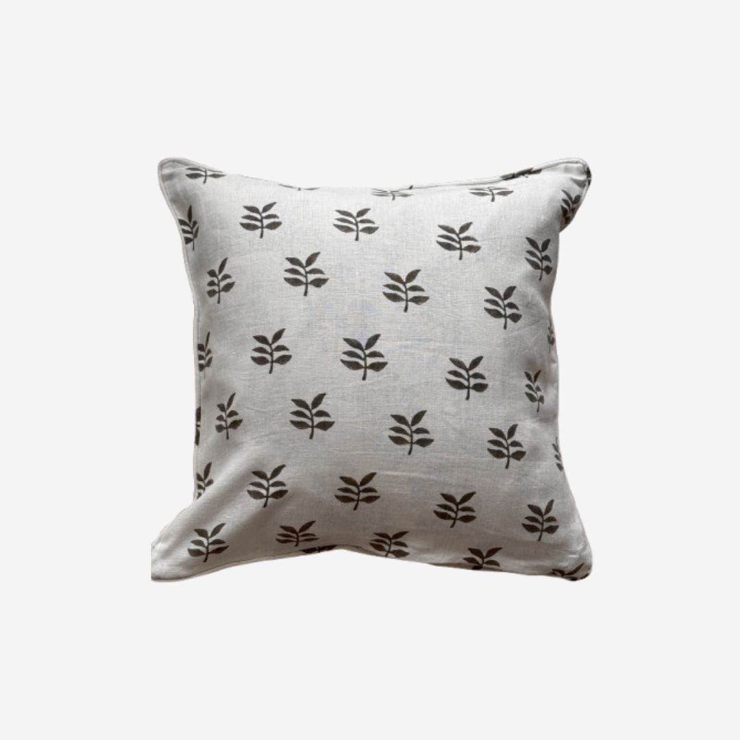 A square throw pillow in a light beige linen fabric with a repeating dark brown leaf pattern, shown against a plain light gray background.