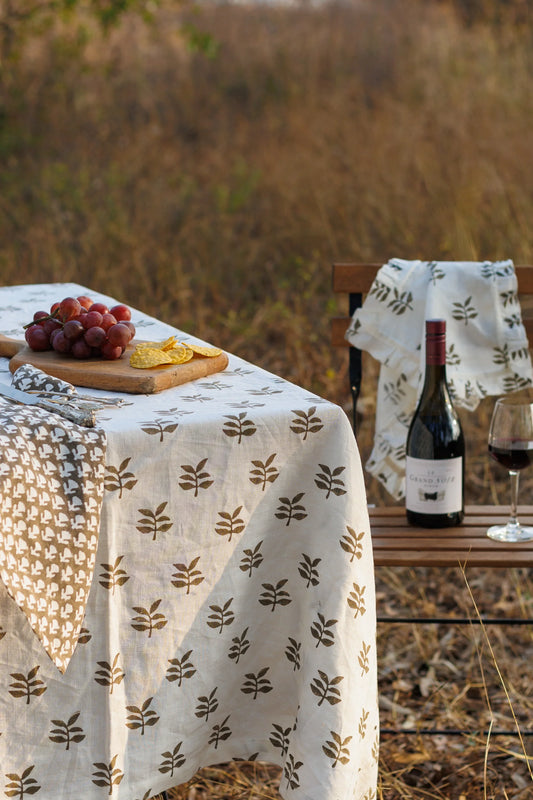 Outdoor setting with a tablecloth, wine bottle, and glass in a natural landscape.