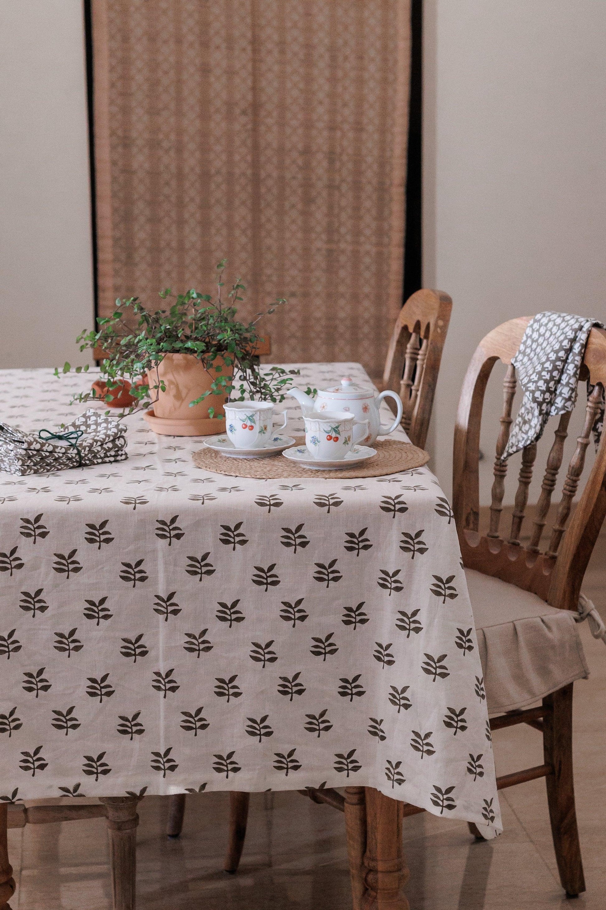 Dining table with a block print patterned linen tablecloth, teacups, and a plant in a room.
