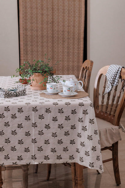 Dining table with a block print patterned linen tablecloth, teacups, and a plant in a room.
