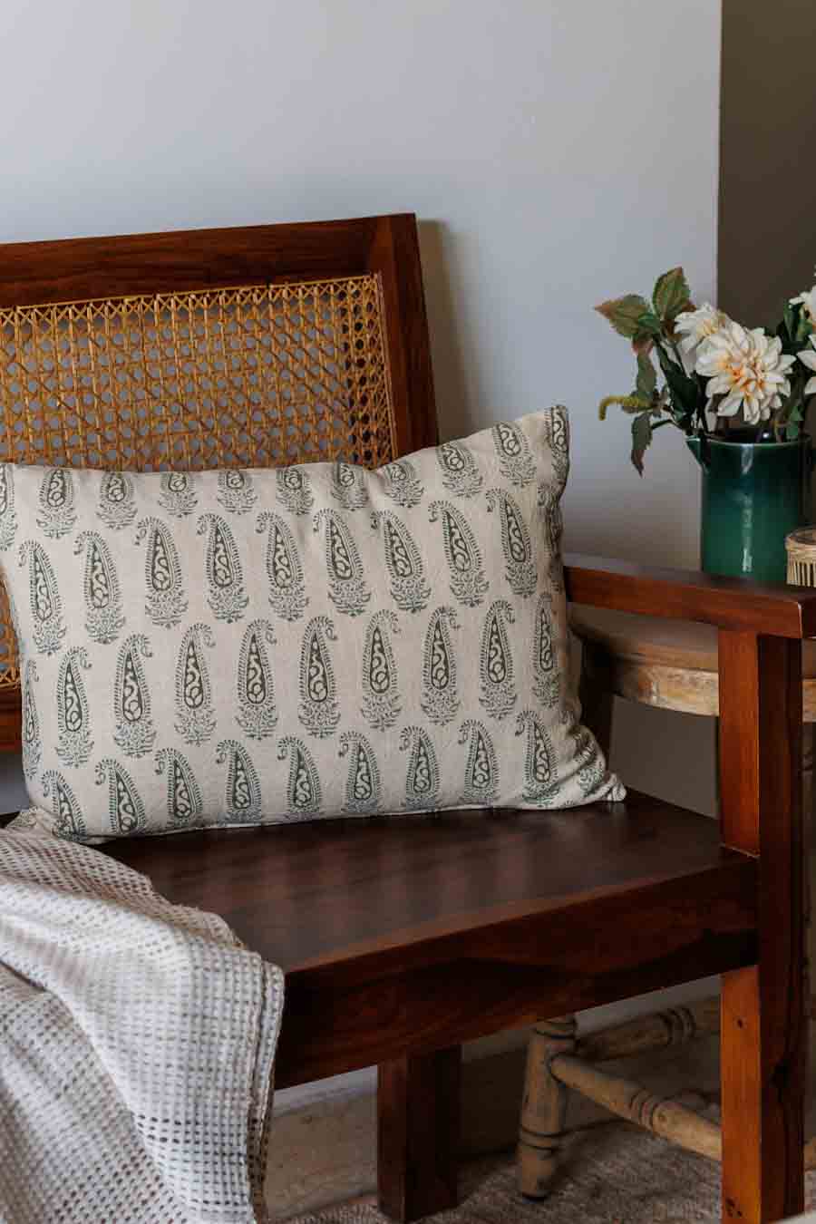 A Lumbar decorative throw pillow with a green paisley block print pattern, resting on a dark brown wooden bench.