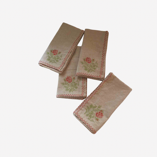 Four beige cross stitch napkins with embroidered floral motifs and checkered borders hero image