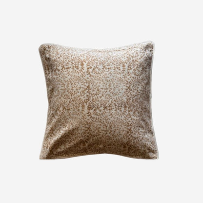 A square cushion featuring block print pattern in shades of brown and beige on a light background, shown against a plain light gray studio backdrop.