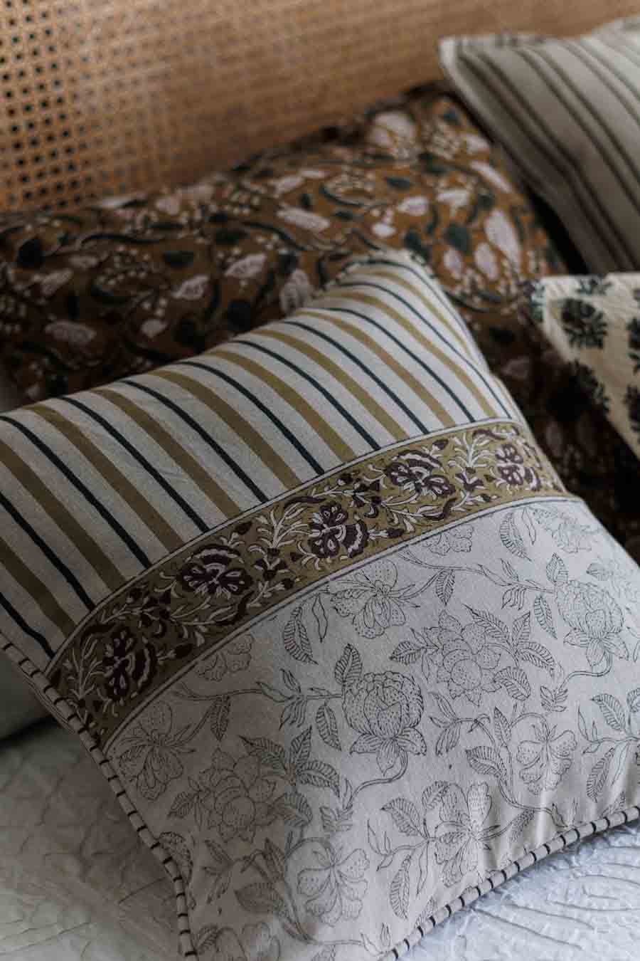 A decorative cushion cover with a striped top section, floral border,  styled on a bed with other pillows.