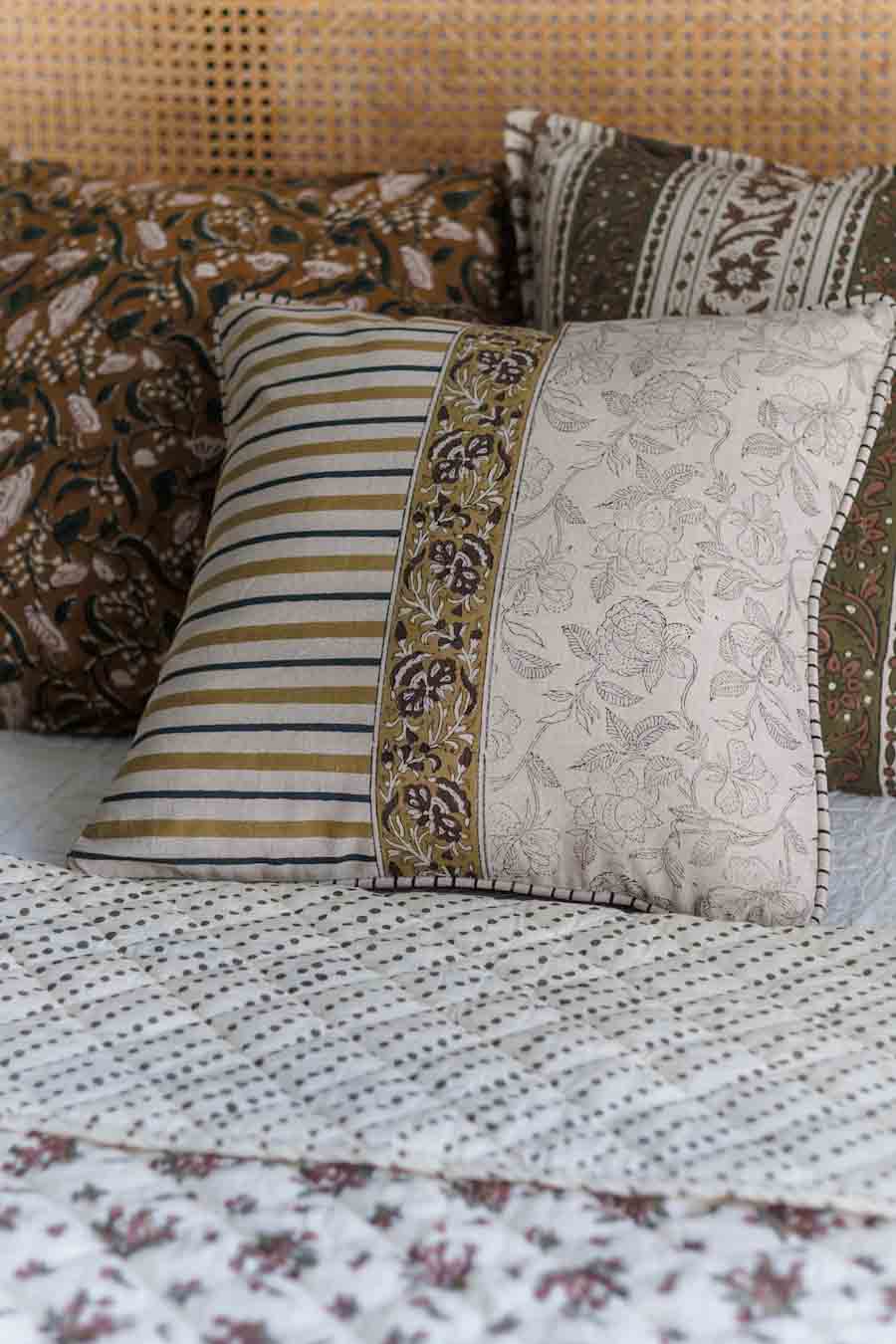 A set of decorative block print cushions arranged on a bed with a block print patterned quilt. 