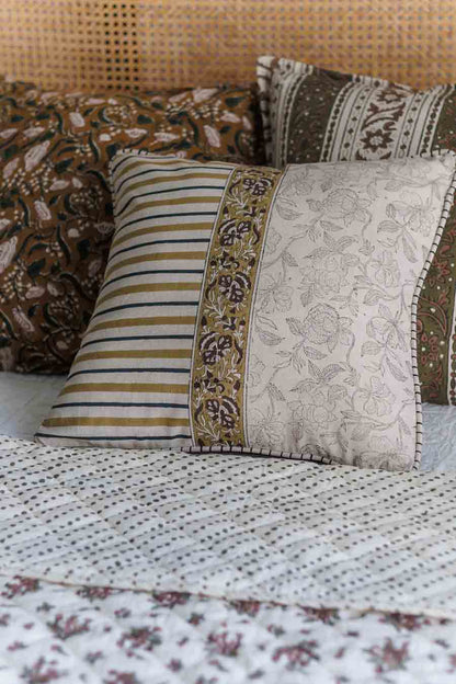 A set of decorative block print cushions arranged on a bed with a block print patterned quilt. 