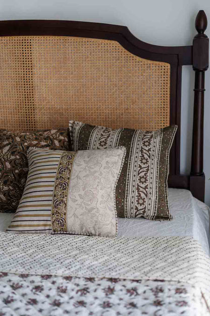A set of block print cushion covers and floral quilt on a rattan bed 