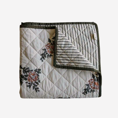 A folded quilted blanket with a cream-colored front featuring a floral pattern in muted red and green, and a striped reverse side with a dark olive green border.